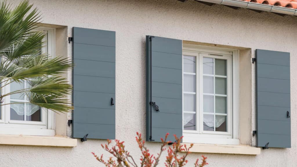 Volets battants gris clair protégeant une maison de la chaleur